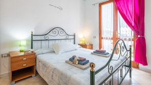 A bedroom with a bed, a nightstand, a lamp, a window with curtains, and a wall with a motivational quote. - Vacation Home "Villa Leonardo Sud Sardegna" with Sea View, Private Terrace & Wi-Fi (Chia)