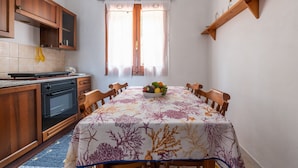 A compact kitchen with wooden cabinets, a built-in oven, and a dining table with a floral tablecloth. - Vacation Home "Villa Leonardo Sud Sardegna" with Sea View, Private Terrace & Wi-Fi (Chia)