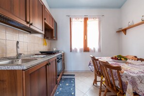Een koelkast, een oven, een kookplaat, kookgerei, borden en bestek
