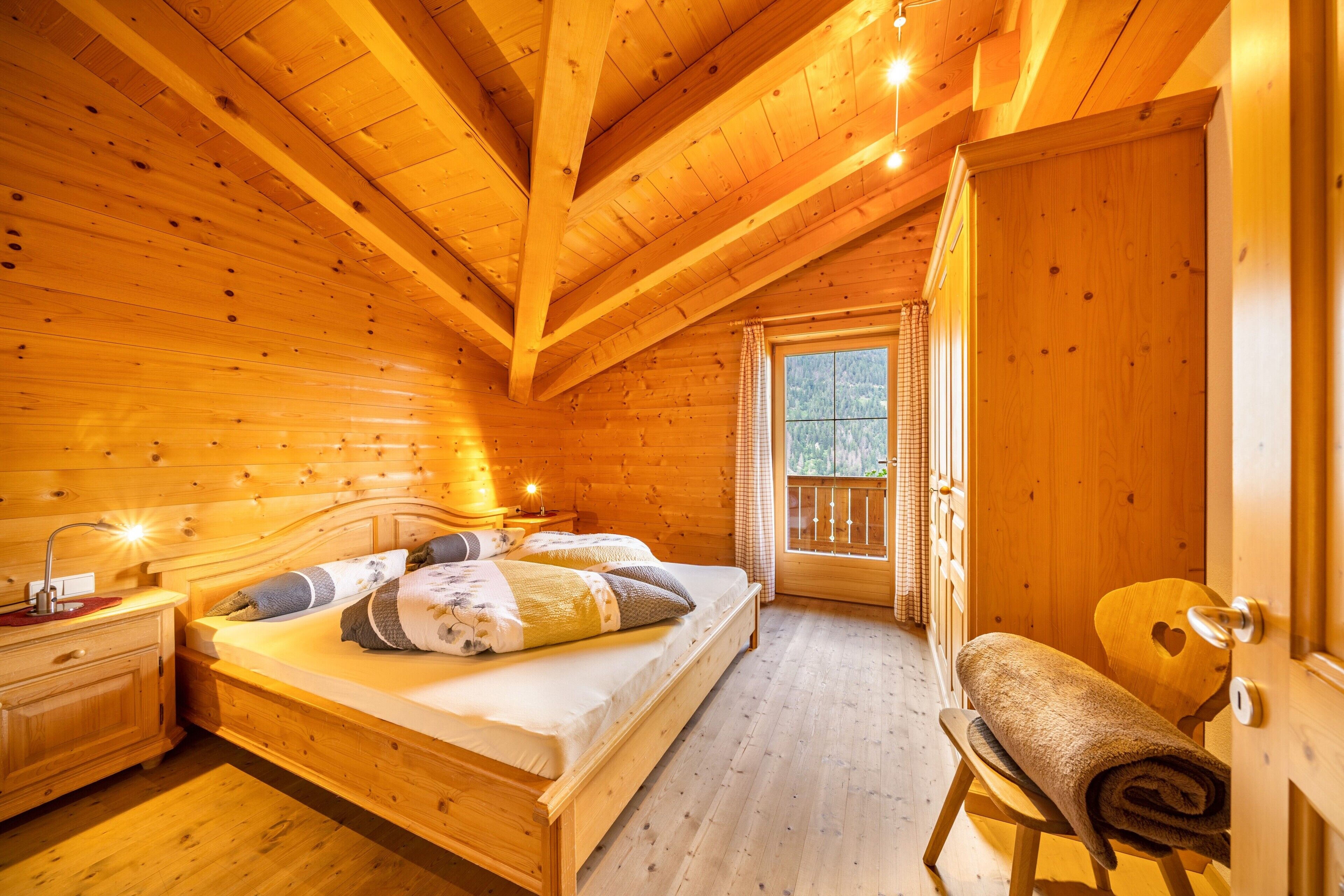 A wooden cabin bedroom with a bed, bedside table, and a window with a view of the outdoors.