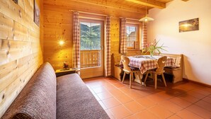 Una baita di legno con un divano, un tavolo da pranzo con sedie e vista sulle montagne attraverso le finestre.
