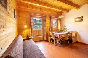 A wooden cabin with a sofa, a dining table with chairs, and a view of the mountains through the windows.
