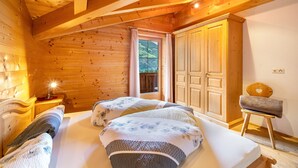 Camera da letto in una baita di legno, con due letti, un comodino, una sedia e un armadio.