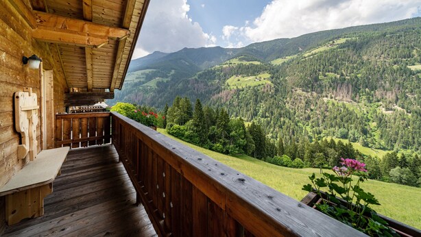 Un balcone in legno con una panchina, vista su un paesaggio montuoso.
