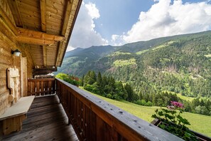 Ein aus Holz gestalteter Balkon mit einer Sitzbank, mit Blick auf eine Berglandschaft.