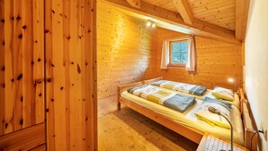 Camera da letto in una baita di legno con un letto a castello, una finestra con tende e un'armadietto in legno.
