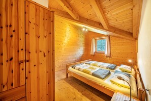 A wooden cabin bedroom with a bunk bed, a window with curtains, and a wooden wardrobe.