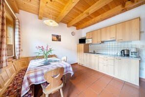 A wooden interior with a dining table, chairs, a clock, and a kitchen area with cabinets and appliances.