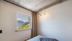 Ein Schlafzimmer mit einem Bett, einem Fenster mit Bergblick und einer Lampe.