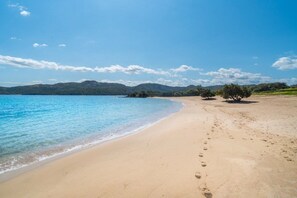 Ein Strand mit klarem, blauem Wasser, sandigem Ufer und fernen Bergen.