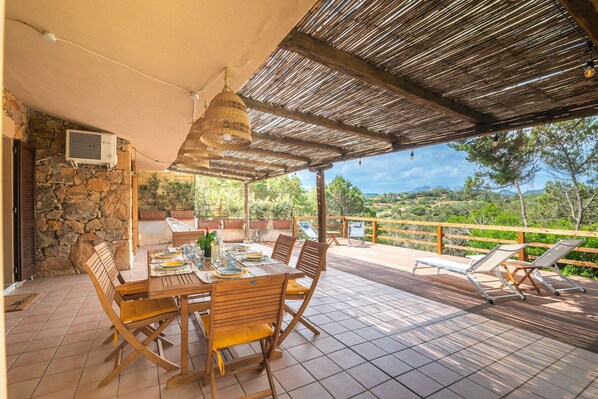 Un patio al aire libre con una mesa lista para comer, un área de estar cubierta y un muro de piedra.