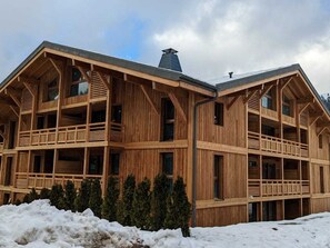 Ein mehrstöckiges Holzgebäude mit Balkonen und großen Fenstern, umgeben von Schnee.