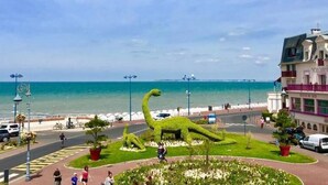 A coastal area with a dinosaur-shaped garden, a road with vehicles, and a building with balconies.