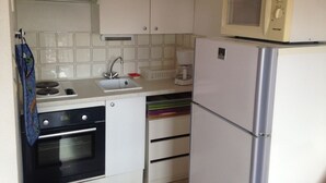 A compact kitchen with white cabinets, a built-in oven, a sink, a microwave, and a refrigerator.