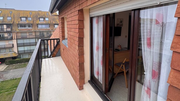 A residential building with a balcony, a sliding glass door, and a view of neighboring buildings.