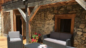 A wooden deck with wicker furniture, a stone wall, and a window. - Cozy apartment for 6 with parking in Grand-Bornand (Le Grand-Bornand)
