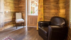A wooden room with a leather chair, a white cushioned chair, and a wooden door with a yellow curtain. - Cozy apartment for 6 with parking in Grand-Bornand (Le Grand-Bornand)