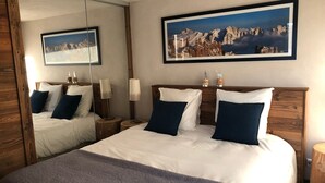A hotel room with a large bed, two bedside tables, a mirror, and a framed picture of mountains. - Cozy apartment for 6 with parking in Grand-Bornand (Le Grand-Bornand)