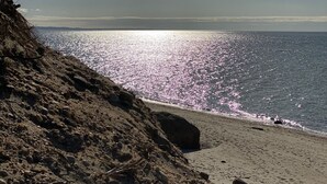 En strand med en stenig förgrund och ett lugnt hav som speglar solljuset.