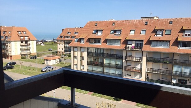 A residential building with multiple balconies, a clear view of the street, and a distant body of water.