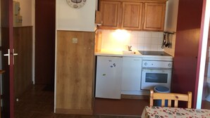 A compact kitchen with wooden cabinets, a refrigerator, a stove, and a clock on the wall.