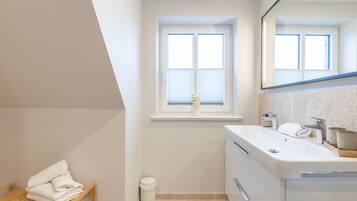 A modern bathroom with a large window, a white sink, and a wooden bench with towels.