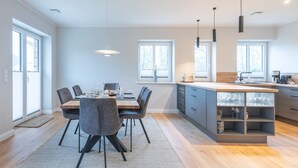 A modern kitchen with a central island, dining area with chairs, and pendant lighting.