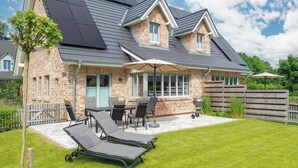 A house with a brick exterior, solar panels, a covered patio, and a lawn with lounge chairs.