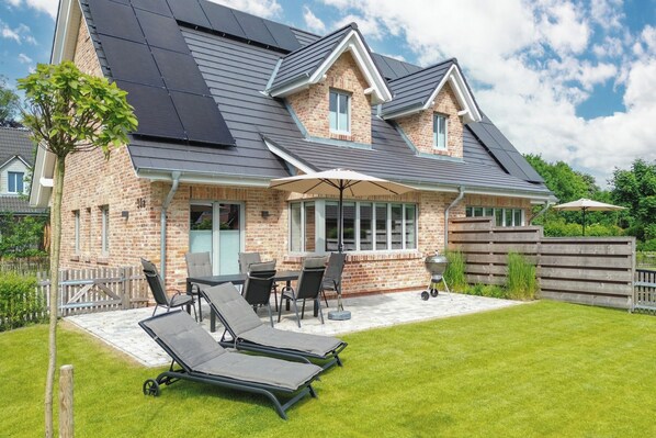 Una casa con fachada de ladrillo, paneles solares, un porche cubierto y un jardín con sillones de descanso.