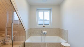 Ein modernes Badezimmer mit Badewanne, einem Fenster und einem Holz-Saunabereich.