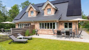 Ein Haus mit Ziegelaußenwand, Solaranlage auf dem Dach, einer Terrasse mit Gartenmöbeln und einem gepflegten Rasen.