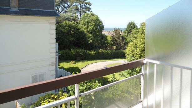 Un balcon offrant une vue dégagée sur un jardin bien entretenu et une vue lointaine sur la mer.