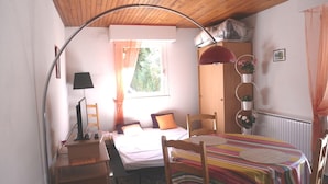 Une chambre confortable avec un lit, un bureau, une chaise, une table recouverte d’une nappe à rayures, une lampe et une fenêtre avec des rideaux.