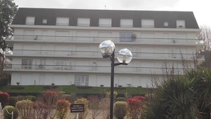 Un immeuble à plusieurs étages, doté d’un toit plat et de balcons. Une enseigne est placée devant l’immeuble, sur laquelle on peut lire : « Annabel et Marie-Camille, prophètes ».
