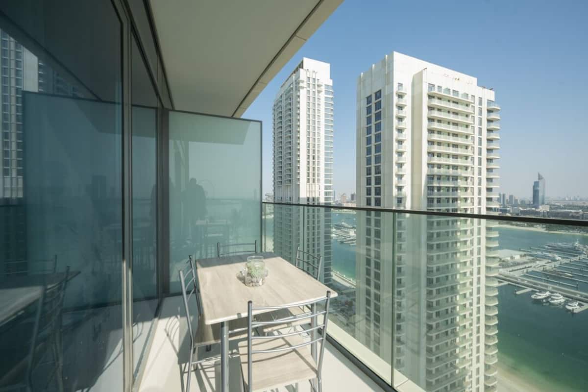 A balcony with a table and chairs, overlooking a marina with tall buildings and a clear sky.