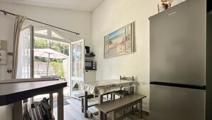 Eine kompakte Küche mit Kühlschrank, Tisch mit Bank, Fenster mit Vorhängen und einem Bild an der Wand.
