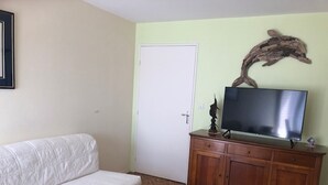 Un salon avec un canapé blanc, un meuble en bois et un téléviseur posé sur un parquet à motifs en chevrons.