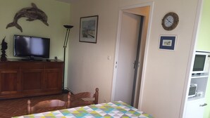Une pièce comprenant une table à manger, des chaises, un téléviseur posé sur un meuble, une horloge et un four à micro-ondes.
