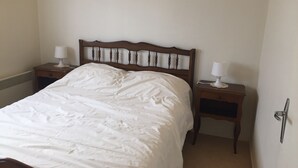 Un lit bien fait, avec une tête de lit en bois, deux tables de chevet avec des lampes et un radiateur fixé au mur.