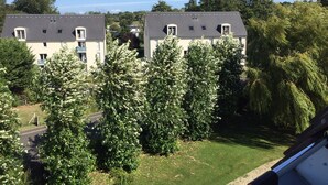 A residential building with multiple windows and a sloped roof, surrounded by lush greenery and trees.