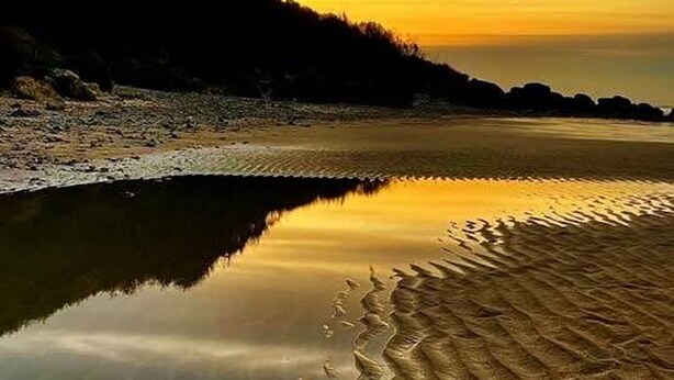 A beach with a calm water surface reflecting the sky.