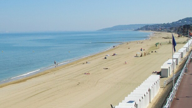 Ein Strand mit weißem Zaun, blauem Himmel und ruhiger See.
