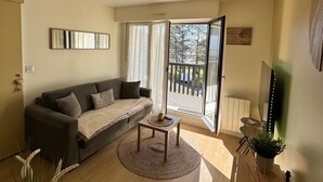 Ein Wohnzimmer mit einer Couch, einem Couchtisch und einem Balkon mit Blick auf Bäume und ein Auto.