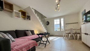 Una sala de estar con un sofá, una mesa de comedor con sillas, una escalera y una zona de cocina.