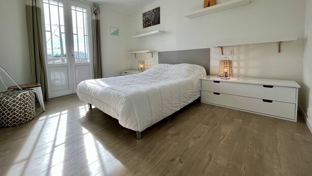 Un dormitorio con cama, mesitas de noche, lámpara colgante y vistas por la ventana.
