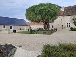 A courtyard with a large tree, a building with a tiled roof, and a solar panel on the left.