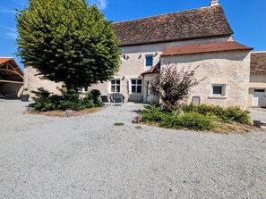 A stone building with a gravel driveway and a large tree in the foreground. - Charming Renovated 11th-Century Cottage near Brenne Ponds - Sleeps 6, Terrace, BBQ, WiFi (Communauté de communes Brenne - Val de Creuse-Douadic)
