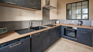 Una cucina moderna con mobili scuri, una cappa aspirante in acciaio inossidabile, una lavastoviglie e un forno integrato.