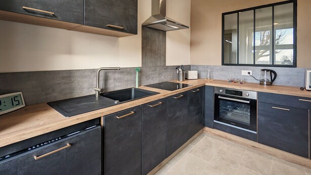 A modern kitchen with dark cabinetry, a stainless steel range hood, a dishwasher, and a built-in oven.
