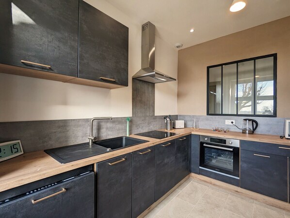 A modern kitchen with dark cabinetry, a stainless steel range hood, a dishwasher, and a built-in oven.